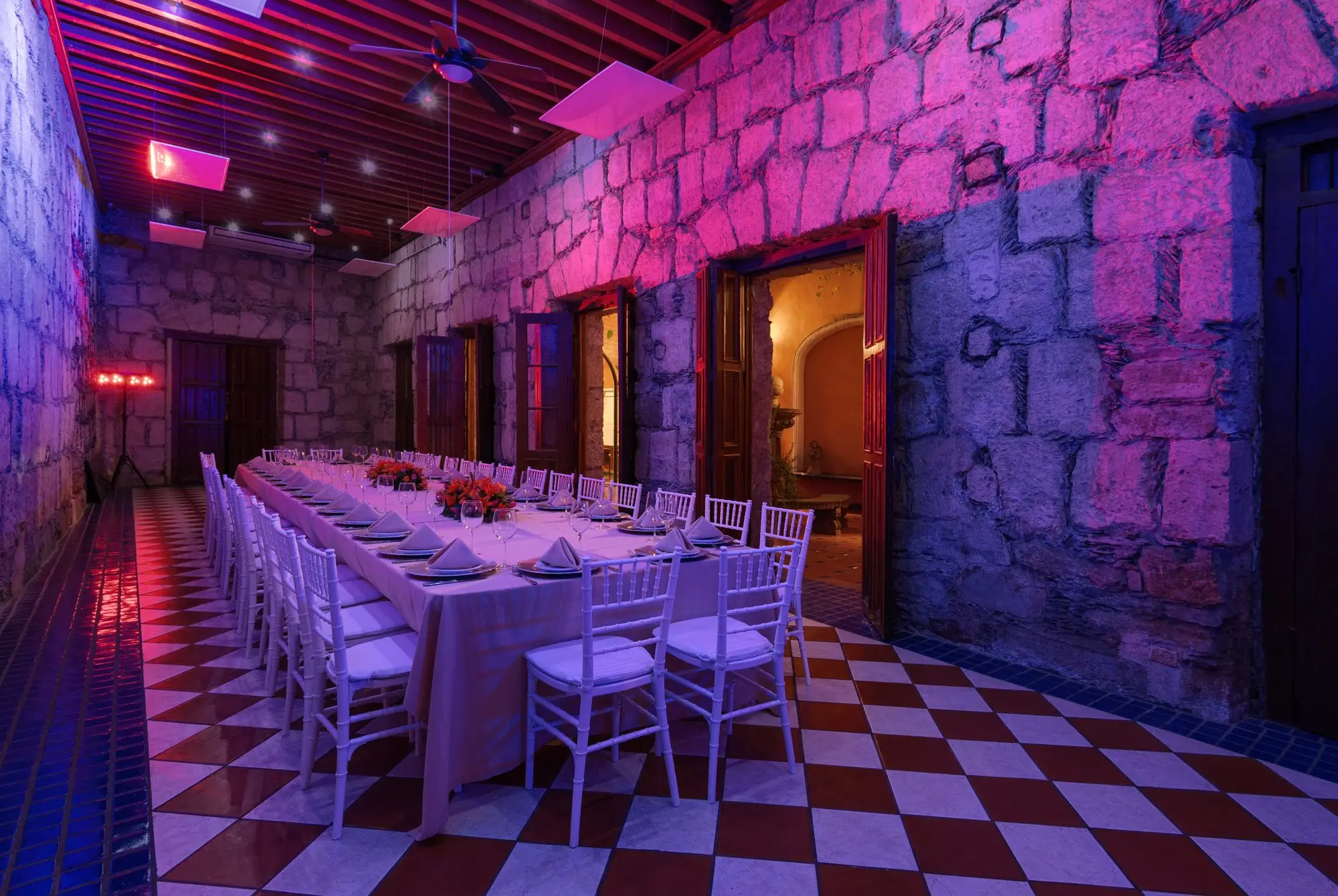 Salón Romancera with mauve lighting on the sandstone walls, set for a long dinner