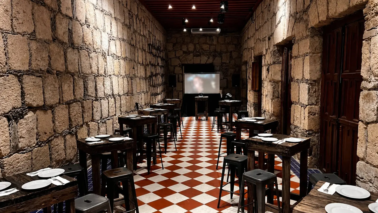 El Salón Romancera en montaje de cóctel, con mesas altas sobre el piso de ajedrez y pantalla al fondo